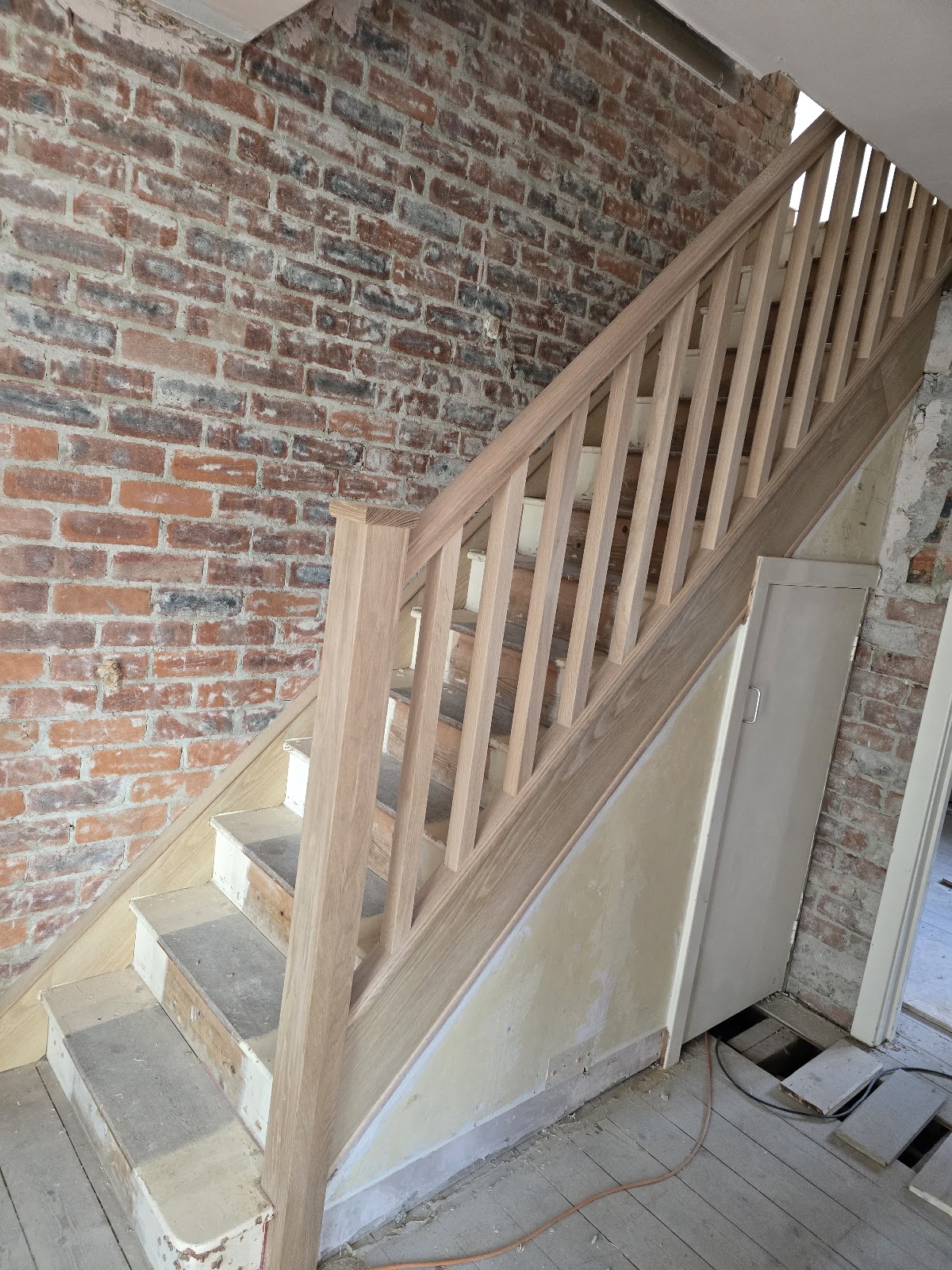 Oak staircase being installed against exposed brickwork